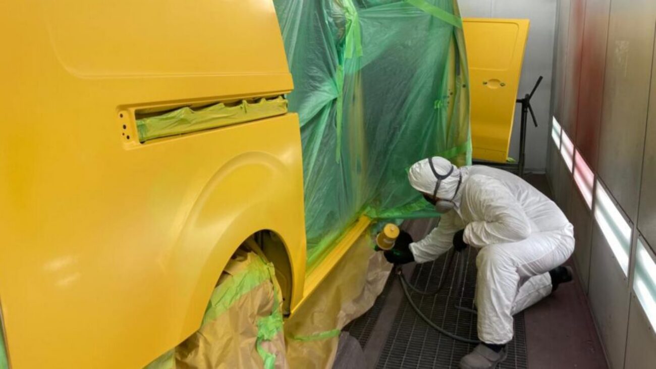 Kratzer im Autolack: Lackierer lackiert ein abgeklebtes Fahrzeugteil in der Lackierkabine